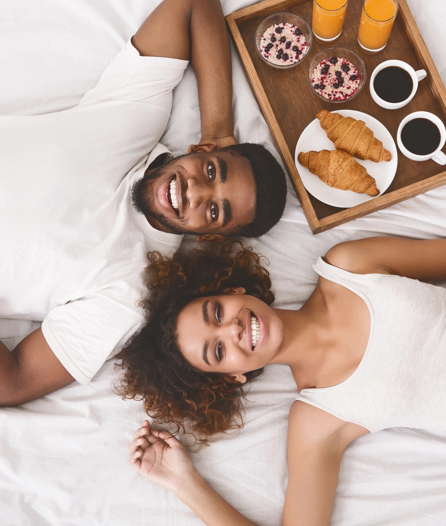 Two people lying in bed with breakfast